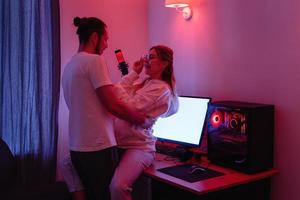 Cheerful couple in room with neon light, having fun on the table with gaming personal computer photo