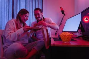 pareja relajándose en casa en una habitación con luz de neón y comiendo pizza, viendo películas en línea o jugando videojuegos foto