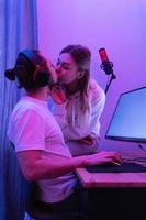 pareja joven besándose en la mesa con computadora personal de juego en luz de neón foto