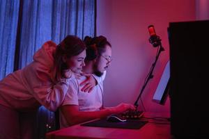 una pareja joven en una habitación con luz de neón está usando una computadora personal moderna foto