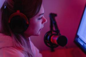 Woman blogger using condenser microphone during online podcast in room with neon light photo