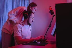 Young couple in room with neon light are using modern personal computer photo