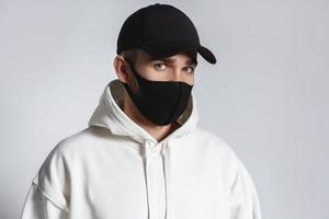 hombre con capucha blanca, gorra de béisbol negra y mascarilla de tela foto