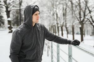 hombre atlético con capucha durante su entrenamiento de invierno en el parque nevado de la ciudad foto