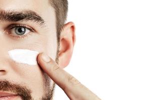 Young man is applying moisturizing and anti aging cream on his face photo