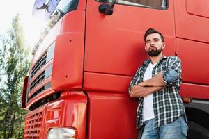 Male truck driver standing beside his red cargo truck photo