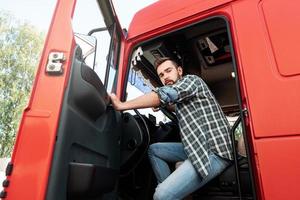 Handsome bearded truck driver inside his red cargo truck photo