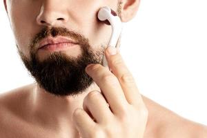 Handsome man using meso roller for better beard growth photo