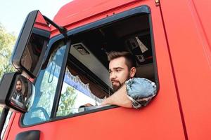 Happy male truck driver inside his red cargo truck photo