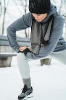 Athletic woman warming up before her jogging workout during winter snowy day in a city park photo