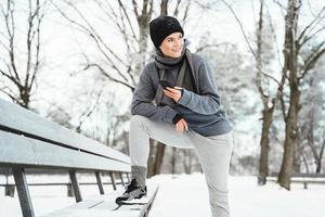 Woman athlete using smartphone during her winter workout in snowy city park photo