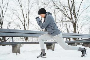 Athletic woman warming up before her jogging workout during winter snowy day in a city park photo