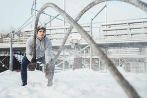 Athlete working out with a battle ropes during snowy winter day photo