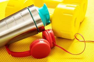 Protein shaker, yellow fitness mat, dumbbells and red headphones. photo