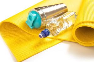 Yellow dumbbells, bottle of water and protein shaker on the fitness mat photo