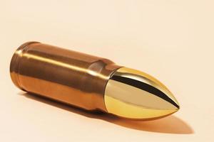 Big and shiny bullet against beige background photo