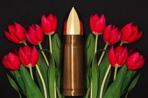 Pacifism, non-violence movement or Victory Day. Bullet and bunch of red tulips.