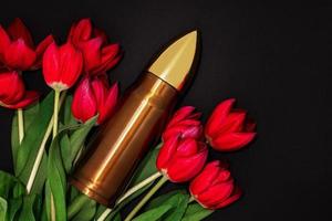 Pacifism, non-violence movement or Victory Day. Bullet and bunch of red tulips. photo