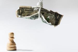 Crumpled one dollar bill hanging on a white rope with wooden chessman standing below. photo