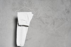 Blank white sweatpants hanging on the thin metallic hanger against light concrete wall photo
