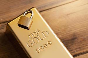 Small brass padlock on a large shiny gold bar. photo