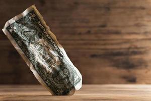 Closeup shot of a crumpled one dollar bill stuck in a gap in the floor. photo