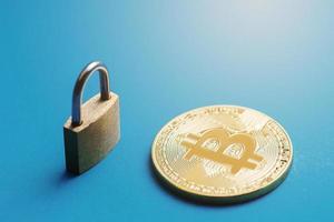 Tiny brass padlock and a shiny golden bitcoin on blue background. photo