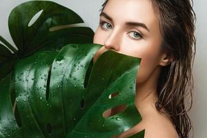 Young woman with a smooth skin holding Monstera deliciosa plant leaf photo