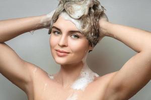 hermosa mujer joven se está lavando el pelo con un champú foto