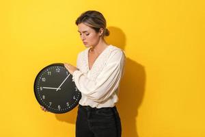 Upset woman holding big clock on yellow background photo