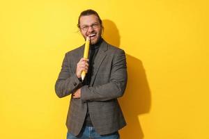 Cheerful man wearing glasses holding big penci on yellow background photo