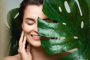 Young woman with a smooth skin holding Monstera deliciosa plant leaf photo