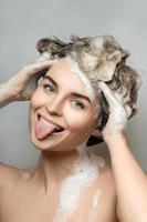 Young beautiful woman sticking her tongue out and washing hair with a shampoo photo