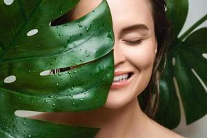 mujer joven con una piel suave que sostiene la hoja de la planta monstera deliciosa foto