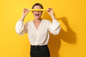 Excited woman covering her eyes with big pencil on yellow background photo