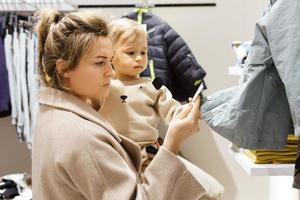 Woman with her baby son choosing clothing in clothes store photo