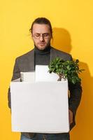 Upset man holding box with personal items after job resignation against yellow background photo