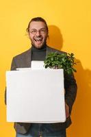 Happy man holding box with personal items after job promotion against yellow background photo