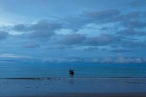 Fishing boat floating in calm sea near sandy beach. photo