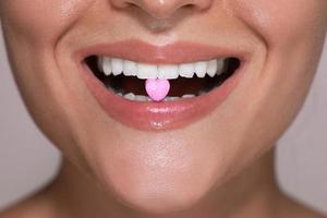 Half of female face with heart shaped pill between teeth. photo