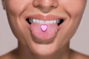 Half of female face with heart shaped pill on tongue. photo