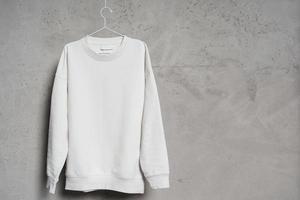 White sweatshirt hanging on the thin metallic hanger against a concrete wall photo