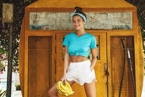 Happy woman with a bunch of bananas posing beside old filling station photo