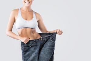 mujer que muestra el resultado después de la pérdida de peso usando jeans viejos foto