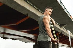 Muscular man during workout with a resistance rubber band on a street. photo