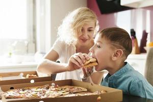 Mother and her cute son eating delicious pizza at home photo