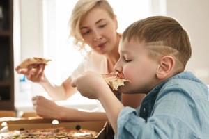 Mother and her cute son eating delicious pizza at home photo