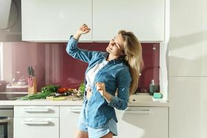 Attractive woman dancing on the kitchen while cooking during sunny morning photo