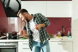 hombre guapo bailando y cantando en la cocina mientras cocina durante la mañana soleada foto