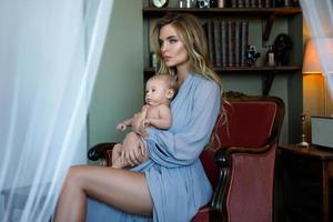 Young beautiful mother wearing luxury grey dress holding her baby on hands photo